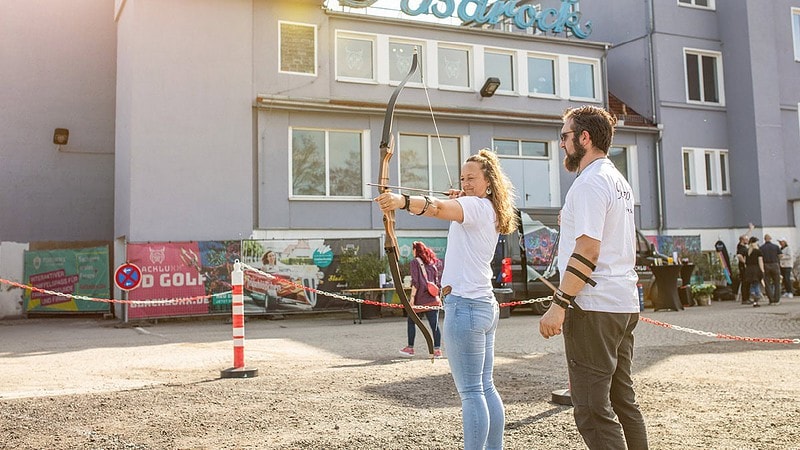 Frau über Bogenschießen und ein Lehrer steht nebenbei