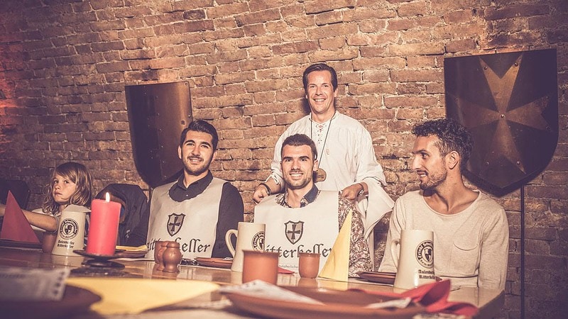 Einem Mann wird eine Schürze vom Ritterkeller angezogen am Tisch