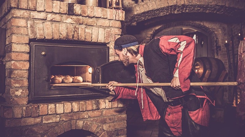 Mann backt Brötchen im Steinofen