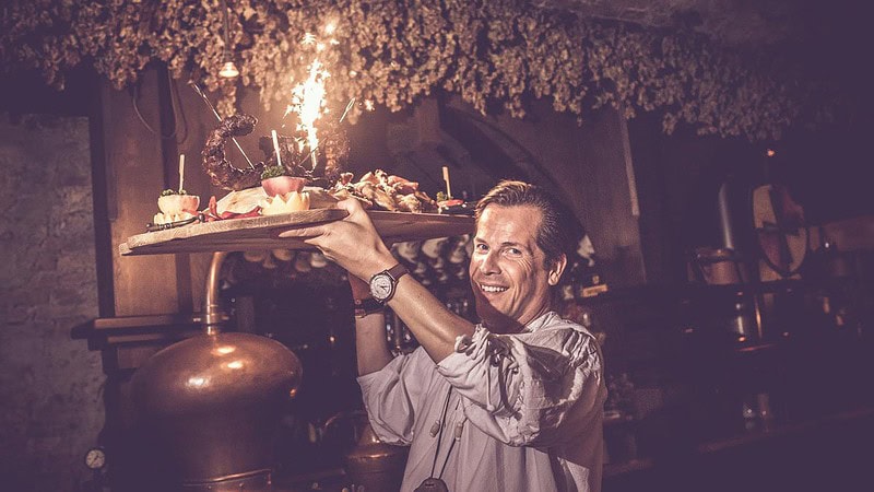 Mann trägt Holzbrett wo sehr viel Essen zubereitet worden ist