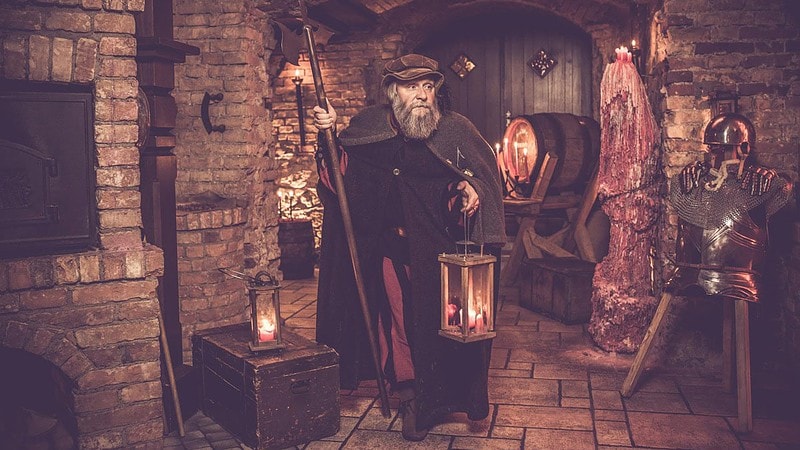 Mann in Nachtwächterkutte mit Mittelalter Ambiente im Hintergrund