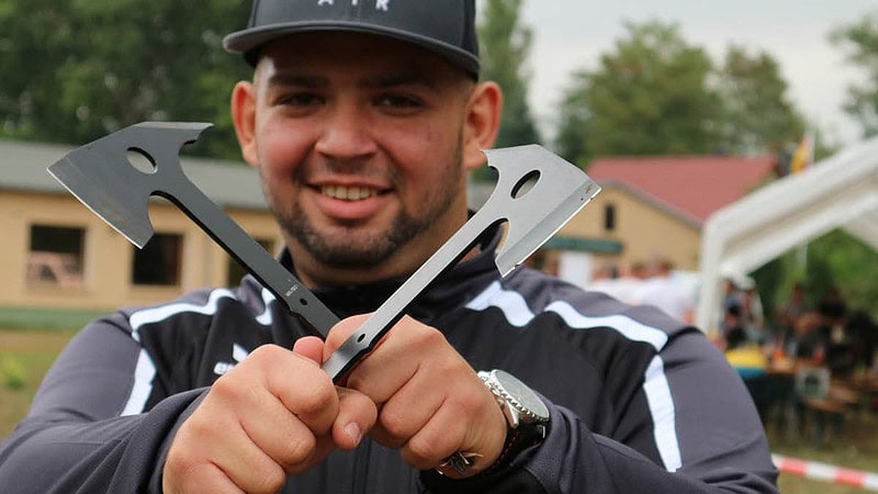 Mann hält zwei Äxte überkreuz vor sich.