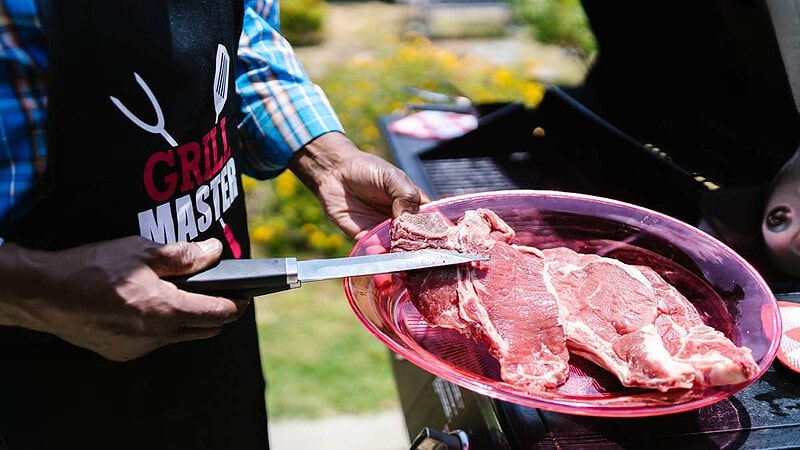 Ein Mann hält einen Teller mit Steak drauf und schneidet es mit einem Messer