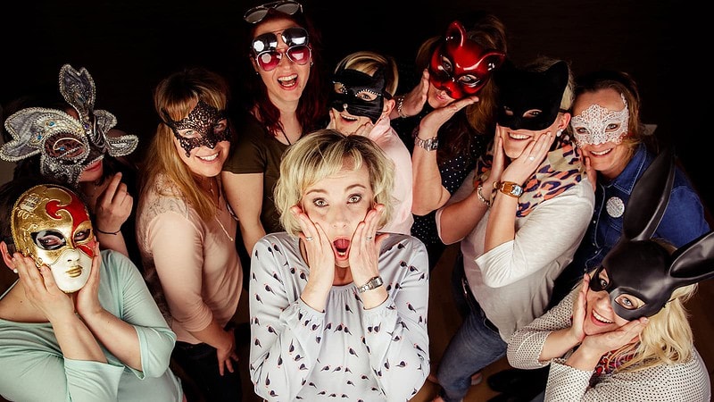 Viele Frauen mit Masten stehen um eine Frau und schauen entsetzt in die Kamera