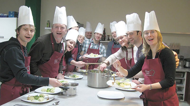 viele Personen stehen am Tisch rund um den Kochtopf beim Kochkurs in Dresden