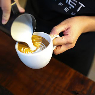 man sieht jemanden, der Milch in eine Tasse kippt- Barista Latte Art Schulung in Dresden