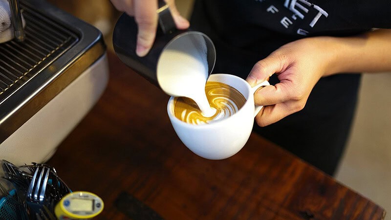 man sieht jemanden, der Milch in eine Tasse kippt- Barista Latte Art Schulung in Dresden