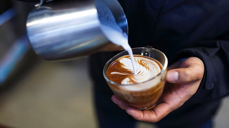 Man sieht jemanden der eine Tasse Kaffee mit Milch vermischt- Barista Latte Art Schulung in Dresden