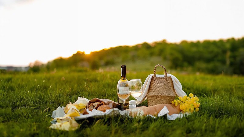 Ein Picknickkorb mit einer Flasche Weißwein, zwei Gläsern sowie anderen Köstlichkeiten auf einer Feldwiese. - Picknick in Dresden