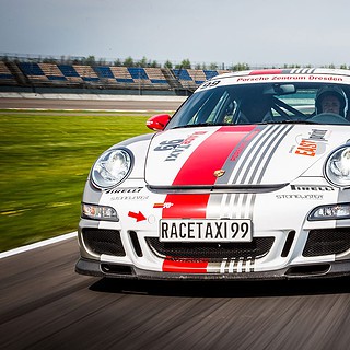 Porsche 911 GT3 fährt auf einer Rennstrecke im Hintergrund weitere Rennwagen sind zu sehen. Der Himmel ist blau.