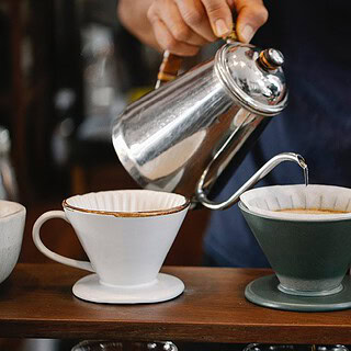 Man sieht eine Hand, die gerade heißes Wasser durch in mehrere Behälter kippt um Kaffee zu filtern- Sensorikkurs mit Cupping in Dresden