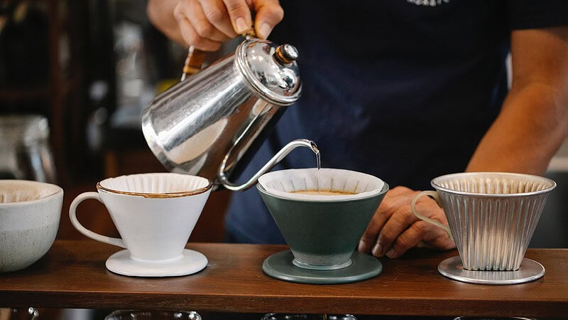 Man sieht eine Hand, die gerade heißes Wasser durch in mehrere Behälter kippt um Kaffee zu filtern- Sensorikkurs mit Cupping in Dresden