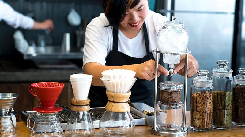 Man sieht eine Frau, die gerade Kaffee durch mehrere Behälter filtert- Sensorikkurs mit Cupping in Dresden