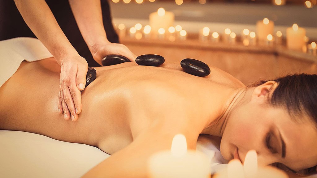 Professional beautician massaging female back by stones