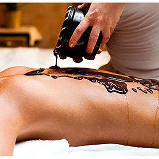 Rücken einer Frau wird mit Moorschlamm begossen für die Erholungs-Moorpackung in Dresden