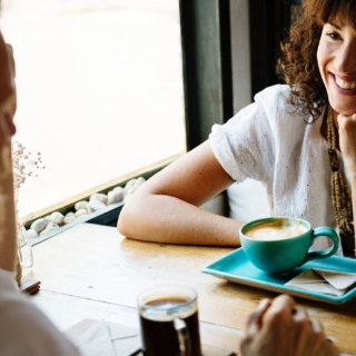 Mann und Frau sitzen am Tisch und trinken Kaffee und lachen zum Speeddating in Sachsen