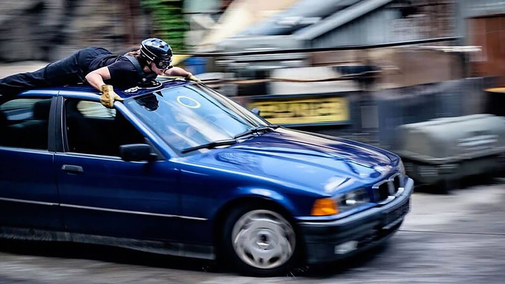 Stuntman-Workshop-in-Babelsberg-Mensch-auf-Auto-im-Vulkan-1.jpg Ein behelmter Stuntman probt eine Szene auf dem Dach eines Autos