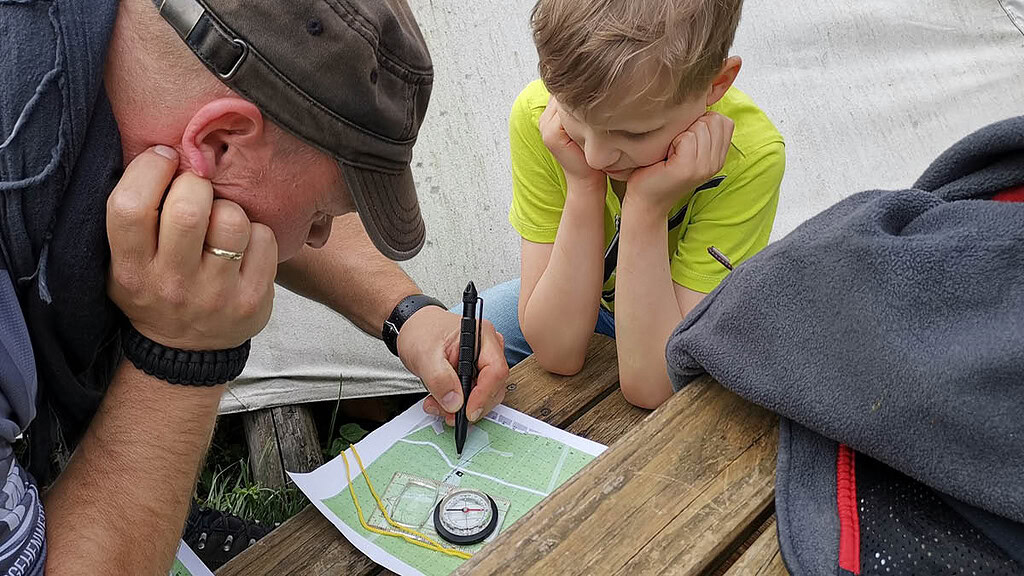 Erwachsener erklärt Kind die Karte mit einem Kompass.