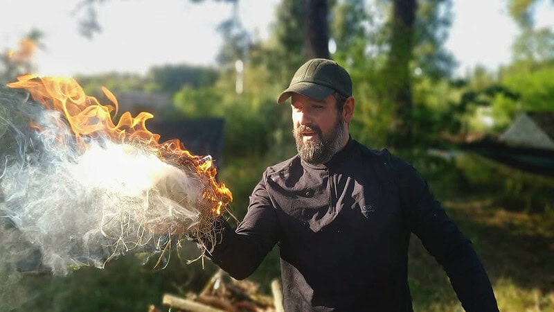Mann hält ein Brennendes Holzwollknäul in der Hand.