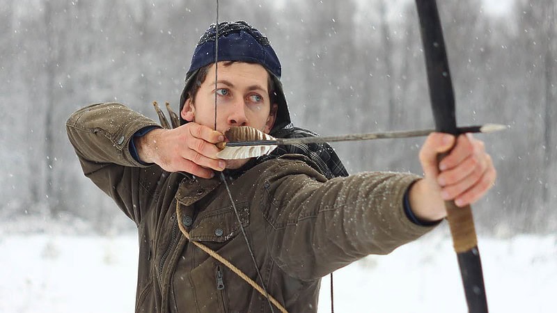 Mann im Winter beim Bogenschießen im Schnee.