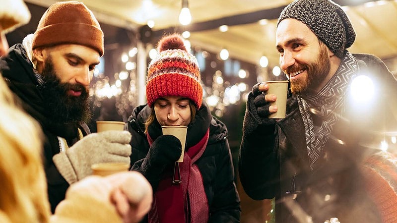 Drei Leute beim Glühwein Trinken in Weihnachtsoutfit.