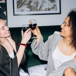 Zwei Frauen feiern zusammen zu Hause und trinken Rotwein