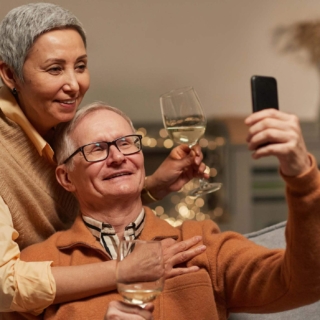 Eine Ehepaar trinkt gemeinsam Weißwein redet mit jemandem auf einem Handy