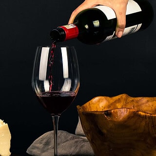 Rotweinglas und verschiedene Käsesorten stehen auf einem Tisch, es ist dunkel, man sieht keinen Hintergrund