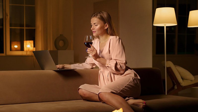 Eine Frau sitzt am Computer und trinkt Rotwein zu Hause