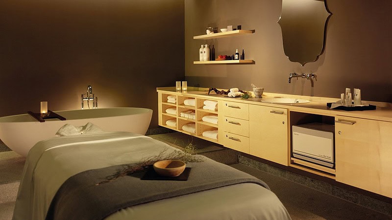 Ein Behandlungszimmer mit einer Badewanne und einer Behandlungsbank auf der eine Schale und Handtücher zu sehen sind.