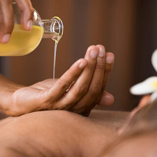 Die Masseurin gibt eine ayurvedische Massage und hält eine Flasche mit Massageöl in der Hand.