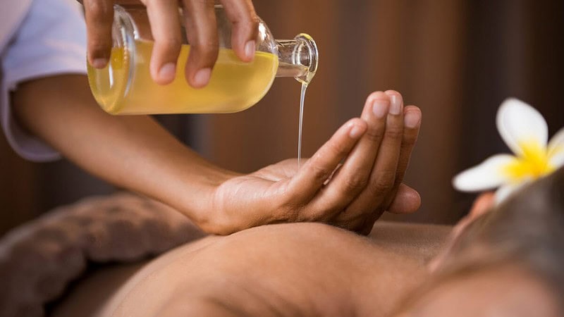 Die Masseurin gibt eine ayurvedische Massage und hält eine Flasche mit Massageöl in der Hand.