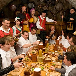 Die Teilnehmer des Ritteressens in München sitzen an der Tafel. Daneben Künstler und Kellner.