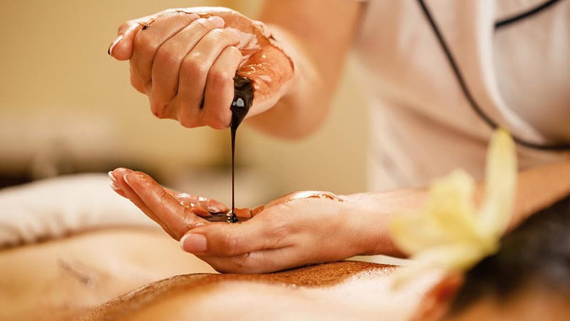 Die Masseurin gießt heiße Schokolade auf den Rücken der Frau, die sie massiert