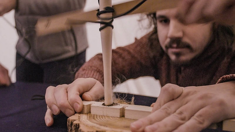 Ein Mann bemüht sich, durch Drehen eines Stocks ein Feuer zu entfachen