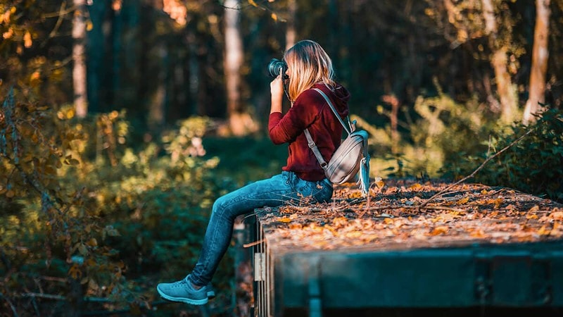 Eine Frau sitzt auf einem Stein am Wald in der Sonne