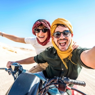 abenteuer-fuer-zwei Ein Paar fährt mit einem Motorrad durch eine Wüste und lächeln