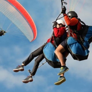 action-geschenke-fuer-maenner 2 Personen fliegen mit einem Gleitschirm, Blick von unten, Himmel und Wolken im Hintergrund
