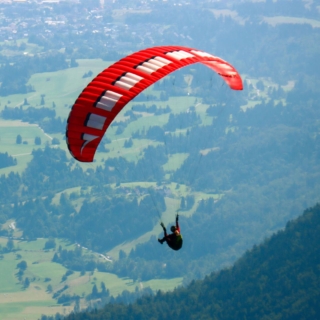 ein Mann fliegt mit einem Gleitschirm über bewaldete Täler