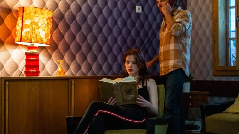 Eine Frau liest ein Buch in einem der Räume im Escape Room, im Hintergrund sucht ein Mann nach Hinweisen