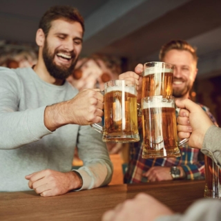 geschenke-fuer-bierliebhaber 3 Männer feiern zusammen in einer Bar und stoßen mit Bier an