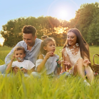 Die Familie sitzt auf einer Decke im Gras und posiert für Fotos, die Kinder spielen mit den Seifenblasen