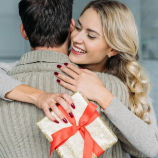 eine Frau erhält ein Überraschungsgeschenk von ihrem Mann, umarmt ihn und lacht