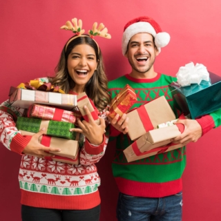 Ein Pärchen posiert für ein Foto mit vielen Geschenken in weihnachtlichen Mützen und Klamotten