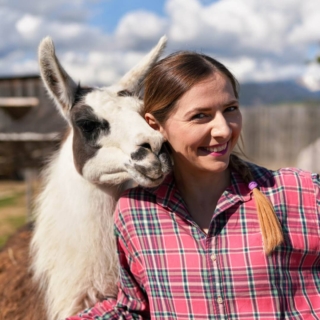 eine Frau kuschelt mit einem Alpaka und lächelt dabei