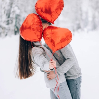 Das Paar posiert für ein Fotoshooting in einer winterlichen Umgebung und drapiert sich in herzförmige Luftballons