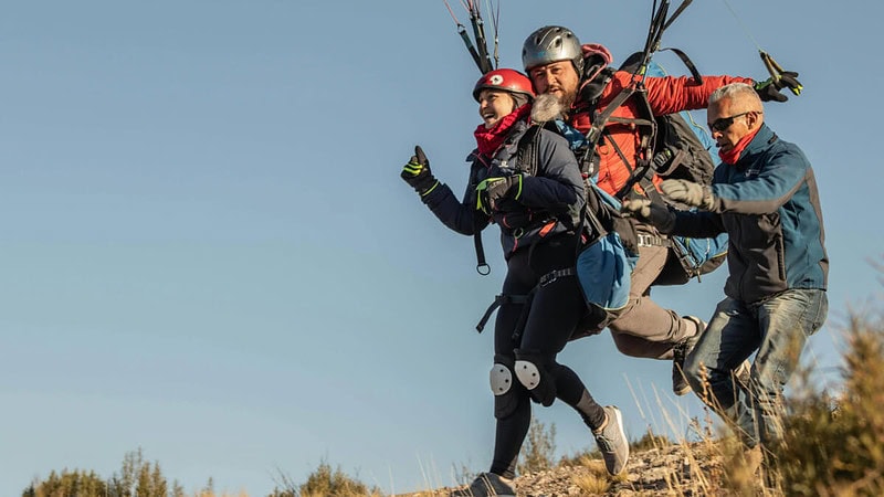 Paar auf dem Gipfel eines Berges, das sich für einen Gleitschirmflug vorbereitet