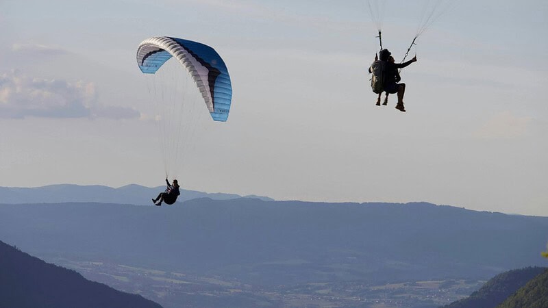 3 Personen fliegen mit zwei Gleitschirmen über die Berge