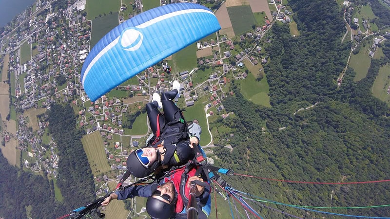 2 Personen fliegen zusammen mit einem Gleitschirm und gucken in die Kamera