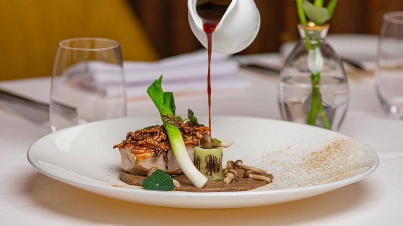 das Steak auf dem Teller mit dem Gemüse wird mit der Sauce übergossen